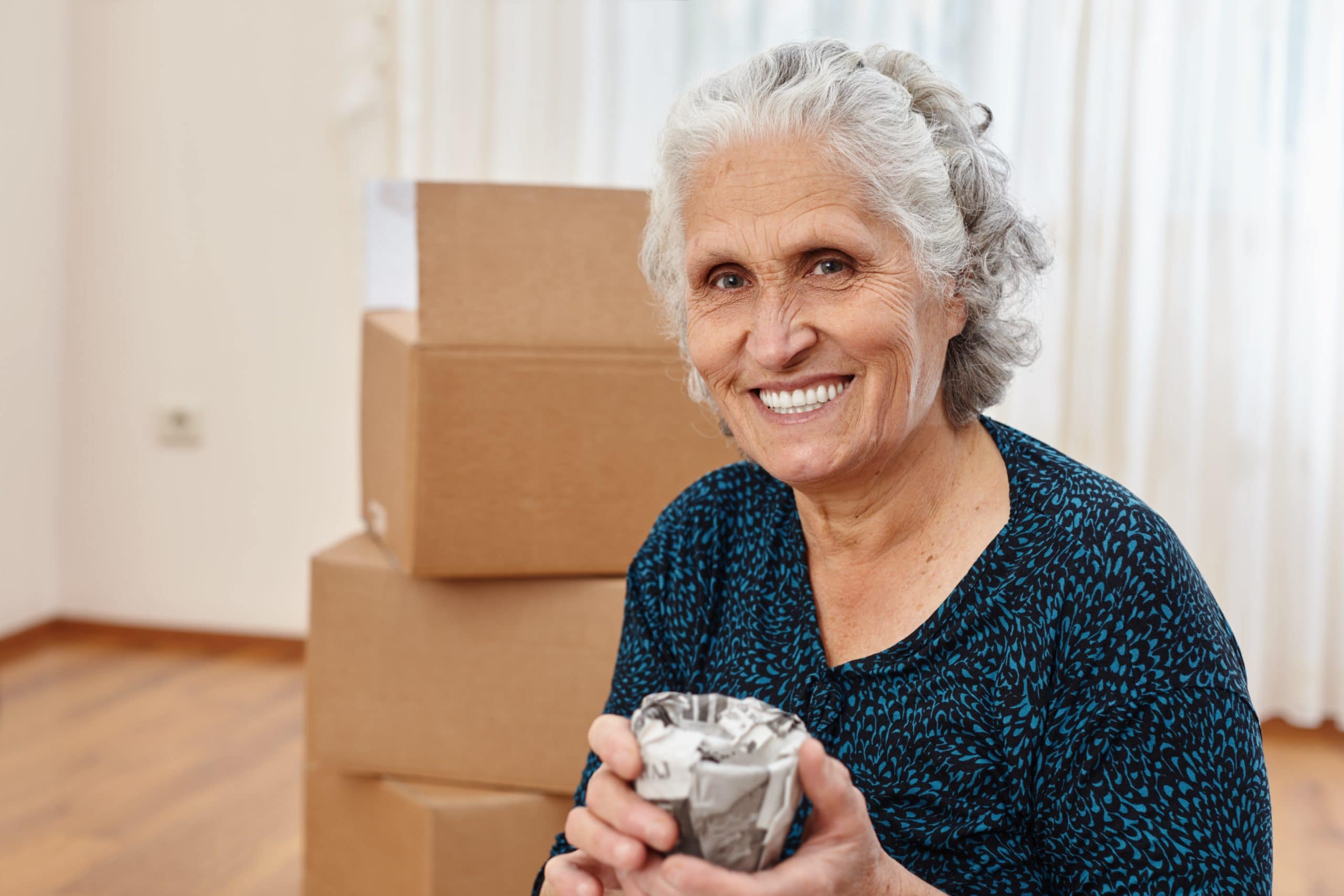 Senior woman smiling with moving boxes in background at Bella Largo.