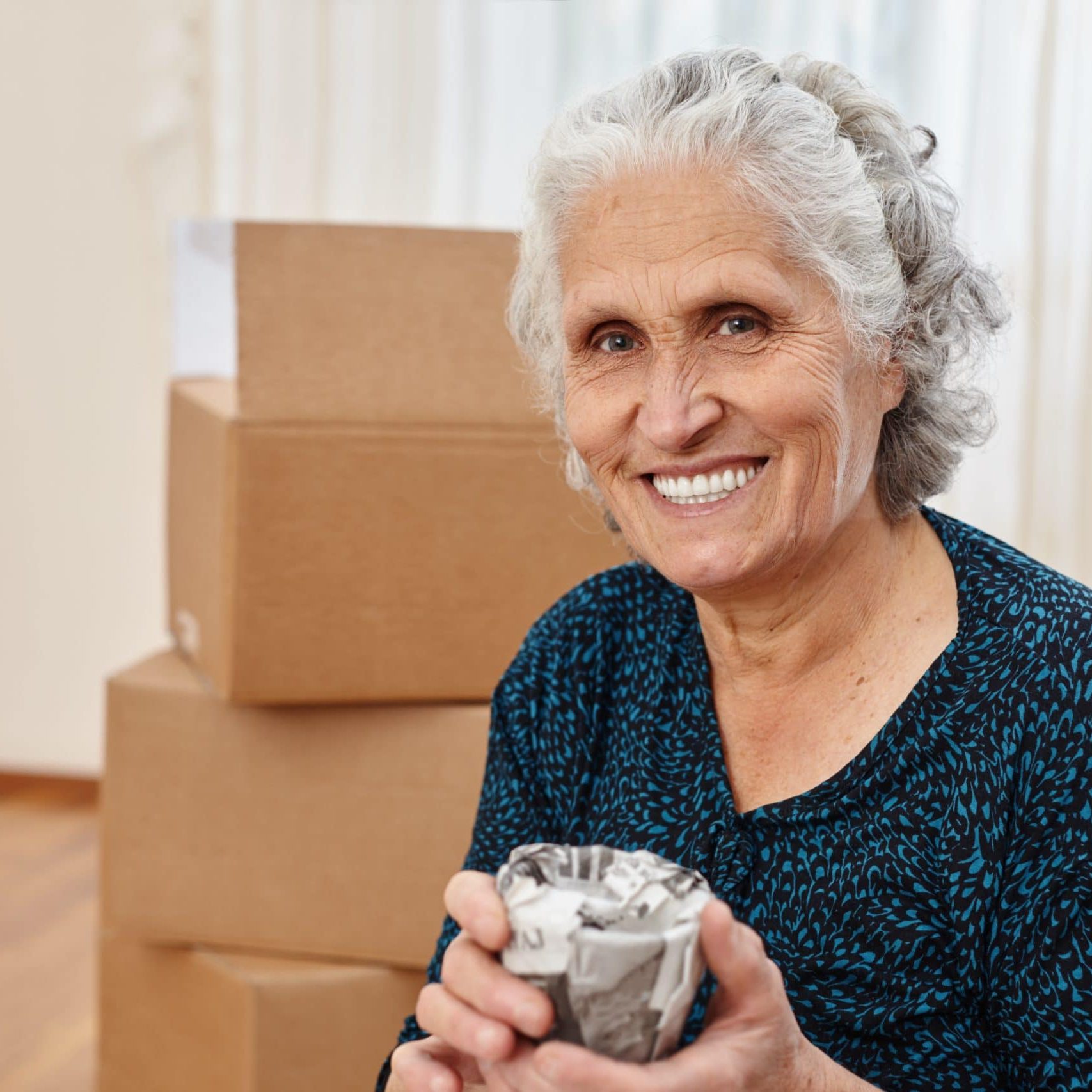 Senior woman smiling with moving boxes in background at Bella Largo.