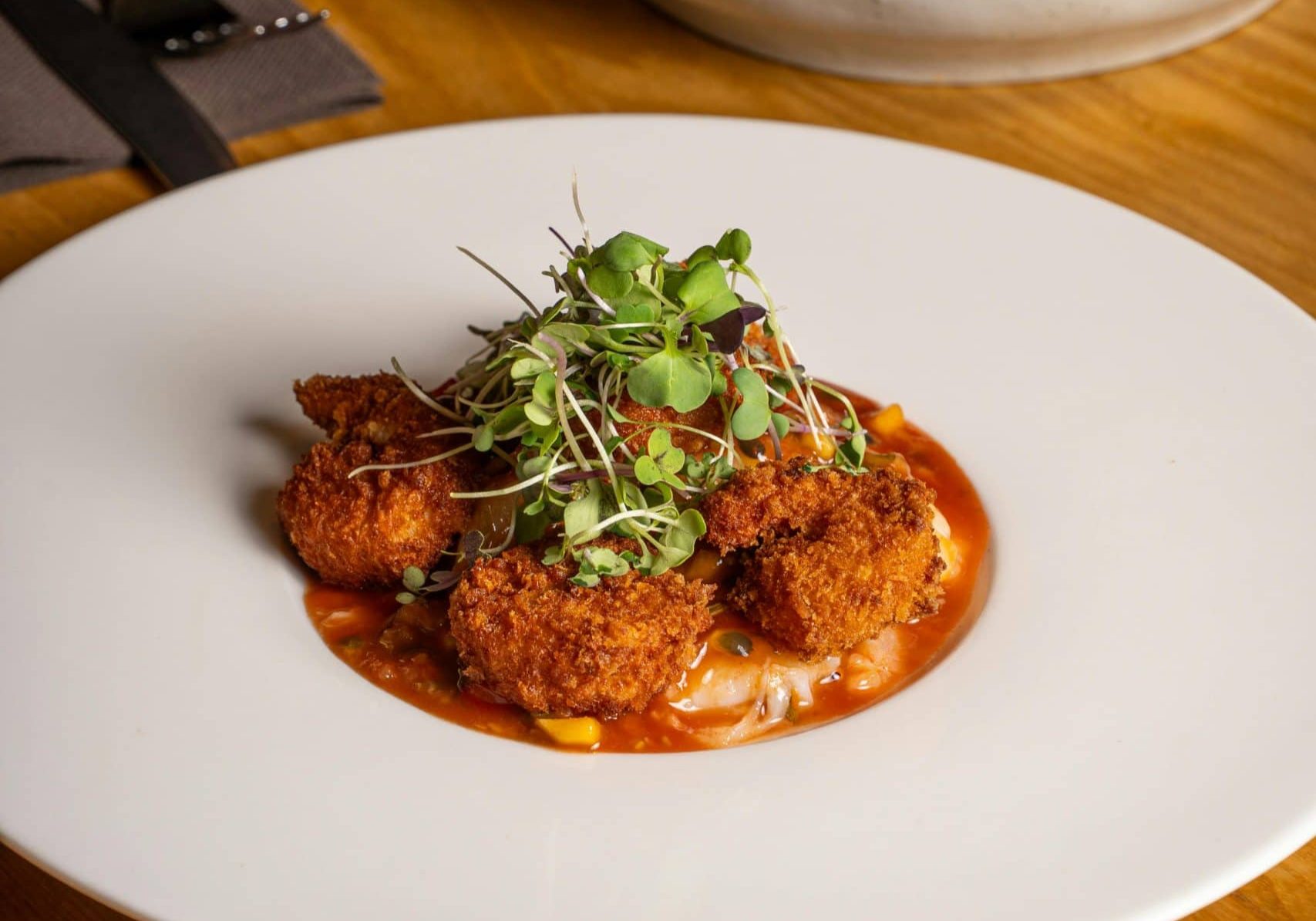 Delicious fried chicken bites topped with microgreens served on a white plate.